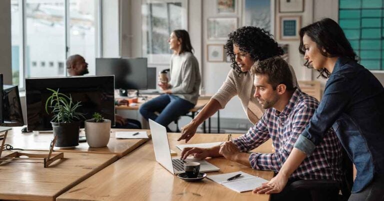 Group of coworkers sitting at a desk, looking at a laptop